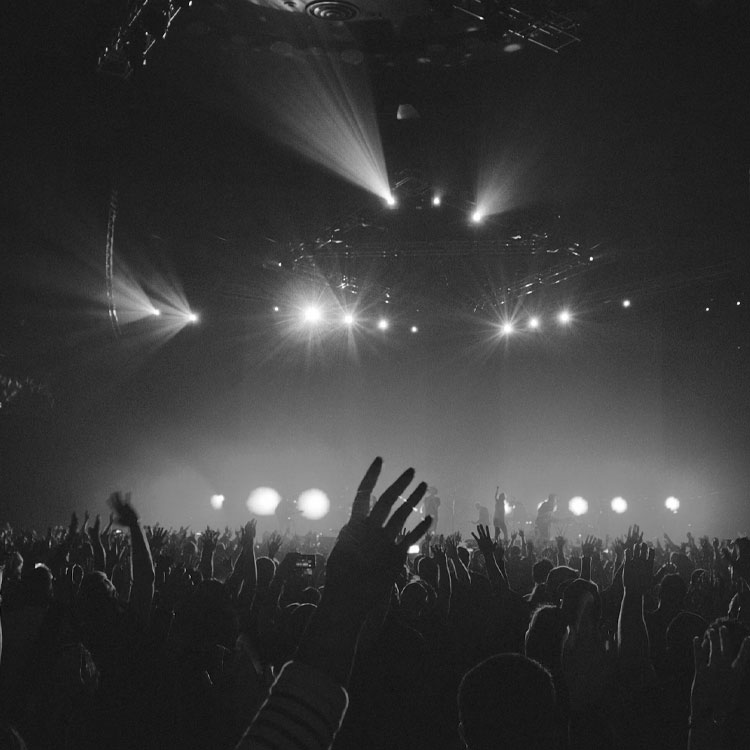 Packed concert venue with an enthusiastic crowd raising their arms in the air.